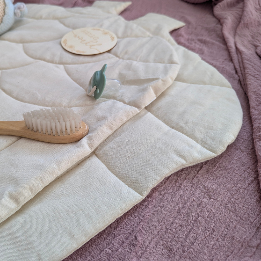 White quilted acorn baby changing mat with wooden items on a pink textured surface
