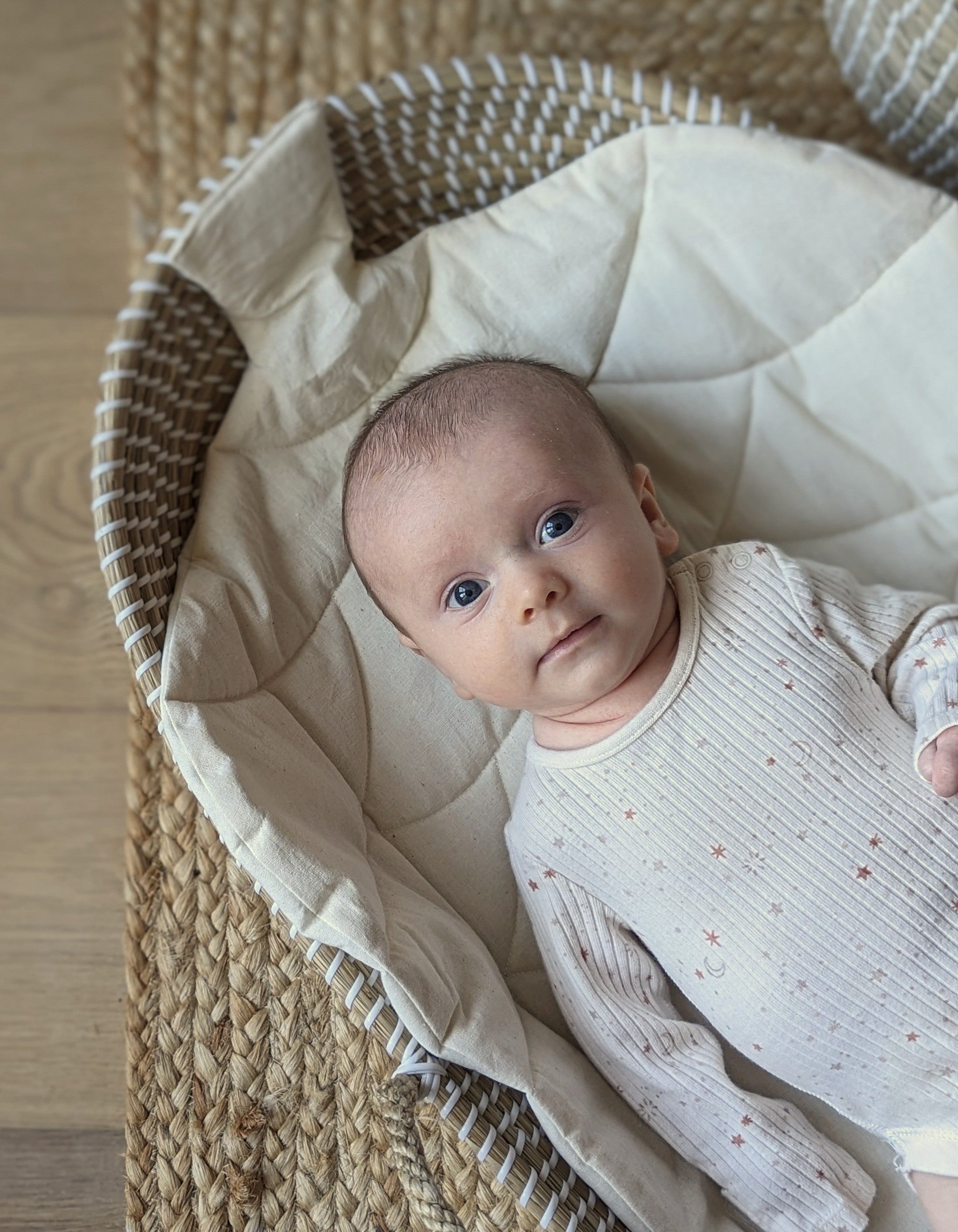 Content smiling baby looking at camera lying on woodland themed acorn mat in handwoven seagrass baby changing basket