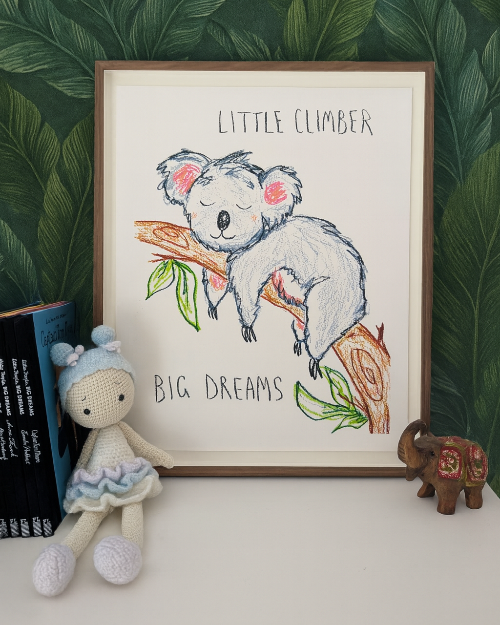 Framed illustration of a koala with 'Little Climber Big Dreams' text, next to a plush toy and small figurine on a leafy background.