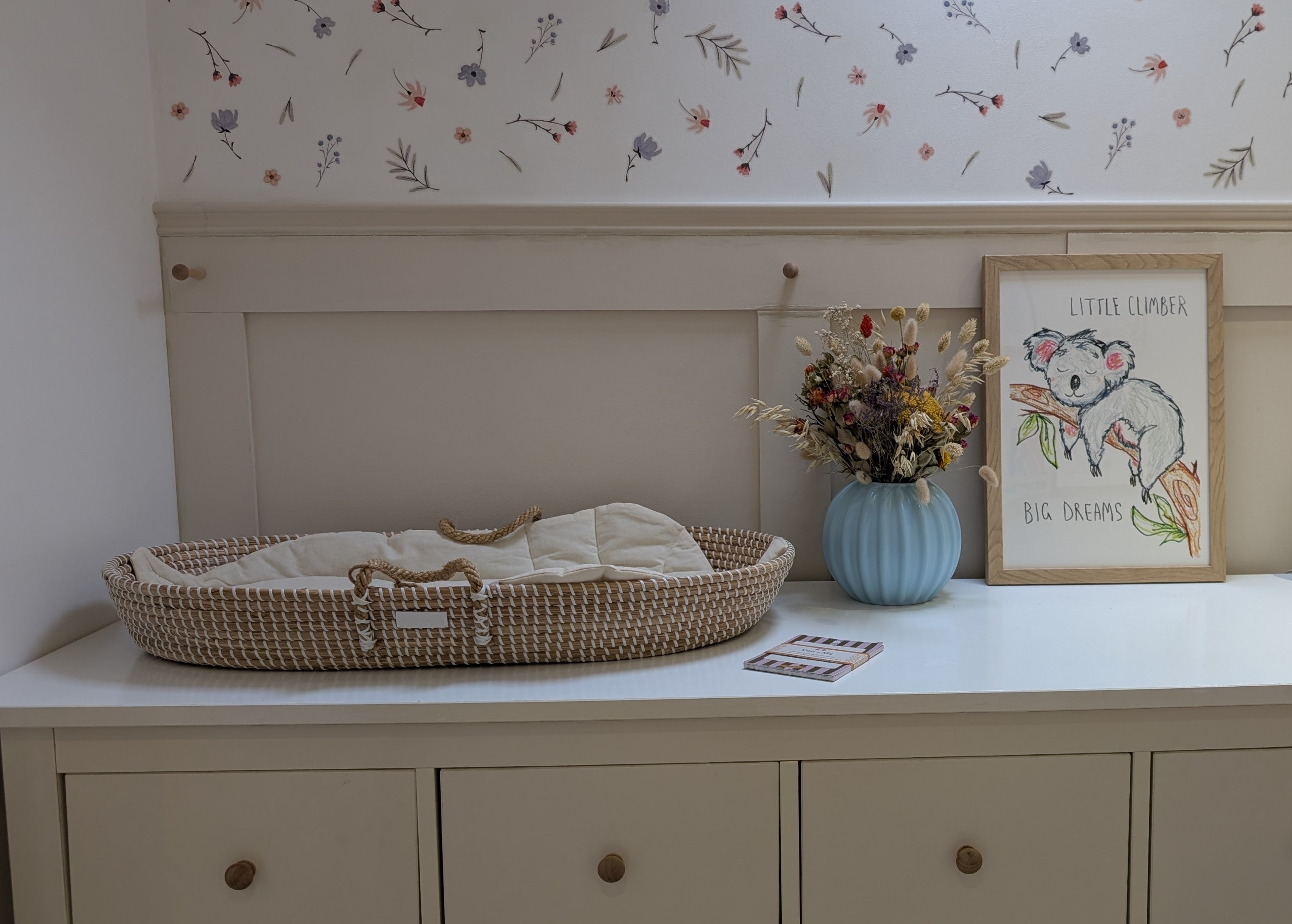 Neutral natural baby changing setup with a seagrass basket and a positive print in an oak frame
