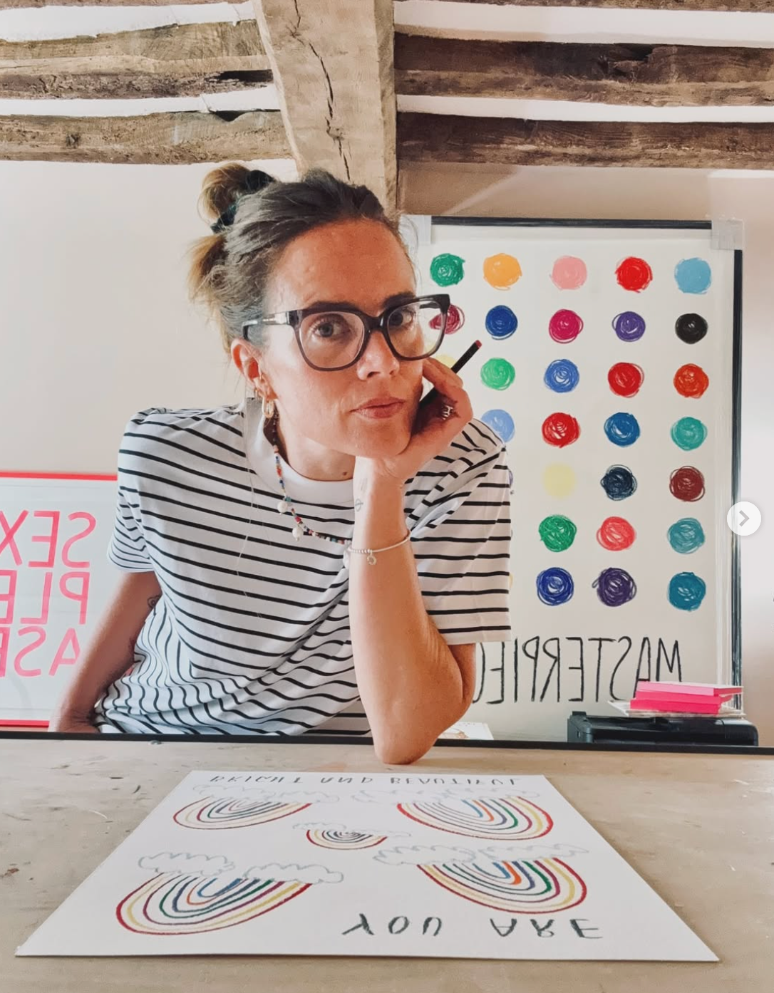 Person sitting at a table with art materials and colorful dot patterns on the wall.