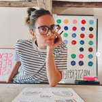 Person sitting at a table with art materials and colorful dot patterns on the wall.
