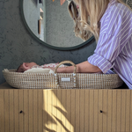 Mum gently soothing her newborn in a natural Moses basket, set on a wooden dresser in a serene, botanical-themed nursery – perfect for mindful pregnancy and early motherhood inspiration.