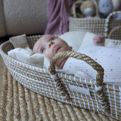 Newborn baby lying in a natural woven Moses basket on a jute rug, wrapped in a soft star-print swaddle – ideal for eco-conscious new mums.